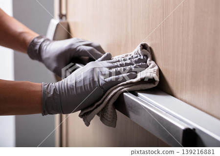 Person wearing grey gloves wipes down a metal door handle with a cloth Person wearing grey gloves wipes down a metal door handle with a cloth 139216881