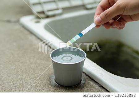 Testing water quality with a pH test strip in a small metal cup near a sink 139216888