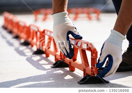 Worker in gloves installs orange plastic barriers for crowd control or construction site safety Worker in gloves installs orange plastic barriers for crowd control or construction site safety 139216898