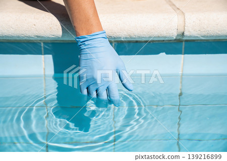 Hand wearing blue glove testing clear swimming pool water for safety and cleanliness Hand wearing blue glove testing clear swimming pool water for safety and cleanliness 139216899