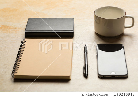 Desk essentials: notebook, pen, smartphone, and coffee mug arranged neatly on a textured surface Desk essentials: notebook, pen, smartphone, and coffee mug arranged neatly on a textured surface 139216913