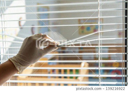 Hand wearing a white glove peeking through window blinds, looking outside 139216922