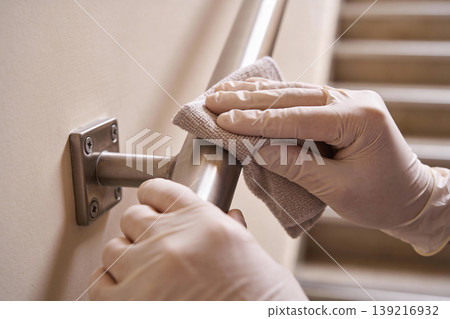 Hands wearing gloves wipe down a metal handrail with a cloth for hygiene and cleanliness Hands wearing gloves wipe down a metal handrail with a cloth for hygiene and cleanliness 139216932