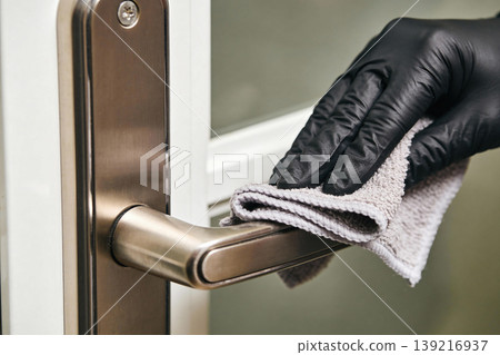 Hand wearing black glove wipes down a metal door handle with a cloth Hand wearing black glove wipes down a metal door handle with a cloth 139216937