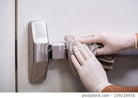 Person in white gloves cleaning a metal emergency exit bar with a cloth Person in white gloves cleaning a metal emergency exit bar with a cloth 139216938