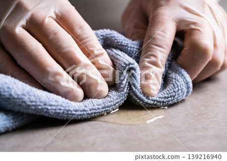 Close-up of hands wearing protective gloves wiping a spill with a blue cloth Close-up of hands wearing protective gloves wiping a spill with a blue cloth 139216940