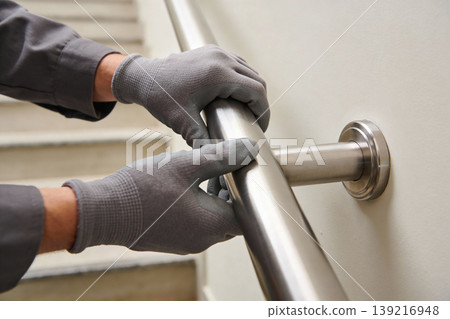 Worker wearing gloves installs a metal handrail on a wall next to stairs Worker wearing gloves installs a metal handrail on a wall next to stairs 139216948