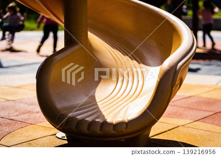Close-up of a bright yellow playground slide with children playing in the background Close-up of a bright yellow playground slide with children playing in the background 139216956