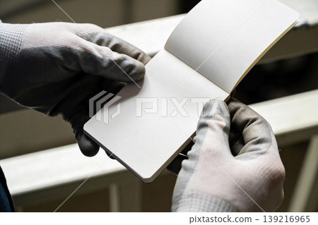 Hands in protective gloves holding an open blank notebook for notes or planning Hands in protective gloves holding an open blank notebook for notes or planning 139216965