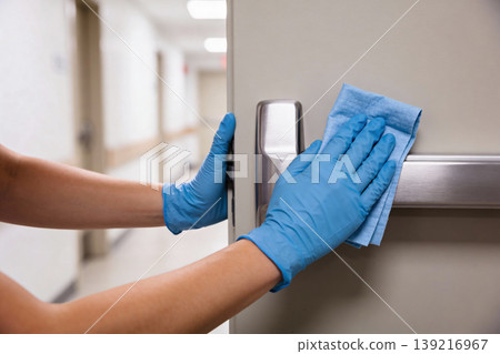 Person in blue gloves cleaning a door handle and bar in a hospital hallway Person in blue gloves cleaning a door handle and bar in a hospital hallway 139216967