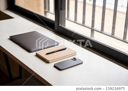 Modern workspace setup with laptop, notebook, and smartphone on a windowsill 139216975