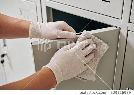 Person wearing white gloves wipes down a metal filing cabinet drawer with a cloth Person wearing white gloves wipes down a metal filing cabinet drawer with a cloth 139216989