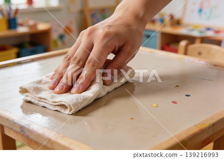 Hand wiping a messy art table with a damp cloth in a classroom setting 139216993