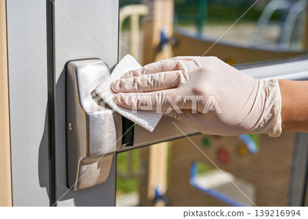 Hand wearing glove wipes down a metal door handle with a wet wipe for hygiene Hand wearing glove wipes down a metal door handle with a wet wipe for hygiene 139216994