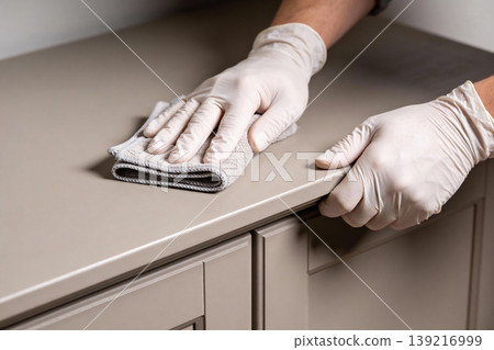Hands wearing white gloves wiping down a beige countertop with a microfiber cloth Hands wearing white gloves wiping down a beige countertop with a microfiber cloth 139216999