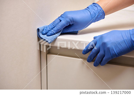 Close-up of hands wearing blue gloves, cleaning a white surface with a microfiber cloth 139217000