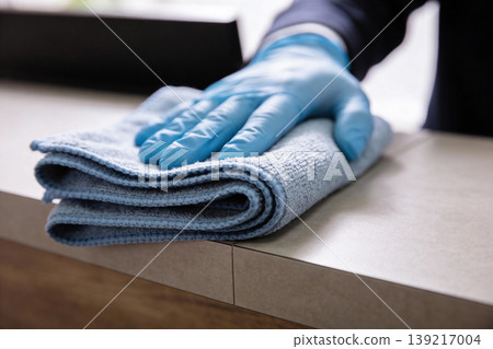 Close-up of a gloved hand wiping a surface with a blue microfiber cloth 139217004