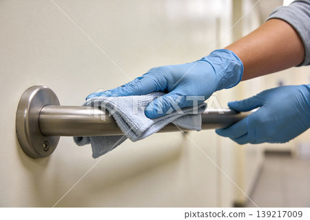 Person in blue gloves cleaning a metal grab bar with a microfiber cloth Person in blue gloves cleaning a metal grab bar with a microfiber cloth 139217009