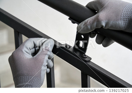Close-up of gloved hands assembling a black metal railing with screws and brackets Close-up of gloved hands assembling a black metal railing with screws and brackets 139217025