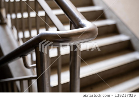 Close-up of a modern metal handrail curving over concrete stairs in a building Close-up of a modern metal handrail curving over concrete stairs in a building 139217029