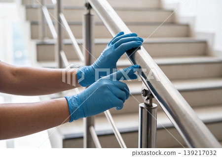 Person wearing blue gloves holding onto a metal handrail on a staircase Person wearing blue gloves holding onto a metal handrail on a staircase 139217032