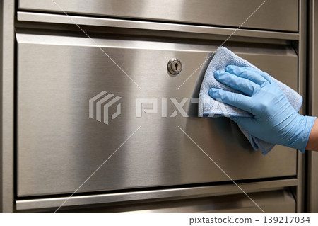 Hand in blue glove cleaning stainless steel surface with microfiber cloth 139217034