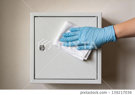Hand wearing blue glove cleaning a metal cabinet with a white cloth 139217036