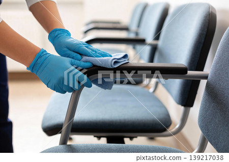 Person in blue gloves cleaning the armrest of a blue chair with a cloth 139217038