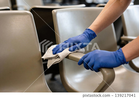 Person in blue gloves cleaning armrest of a chair with a cloth Person in blue gloves cleaning armrest of a chair with a cloth 139217041