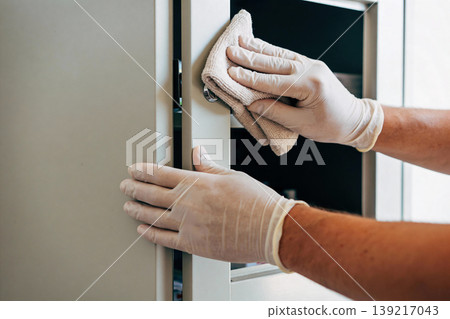Person wearing gloves wipes down a metal cabinet with a cloth for hygiene and cleanliness Person wearing gloves wipes down a metal cabinet with a cloth for hygiene and cleanliness 139217043