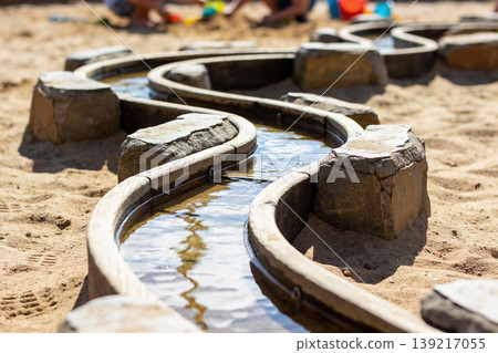 Curving wooden water channel with stone supports carved in sand at family beach play area 139217055