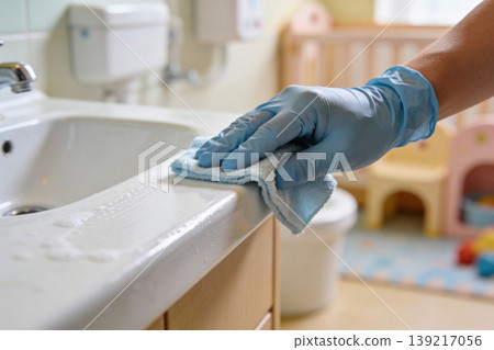 Hand wearing blue glove wiping down a bathroom sink counter with a blue cloth Hand wearing blue glove wiping down a bathroom sink counter with a blue cloth 139217056