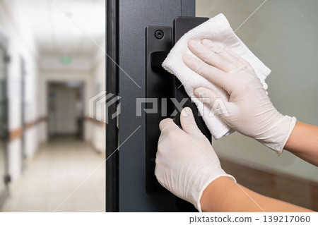 Hands in gloves cleaning a door handle with a cloth in a hospital hallway Hands in gloves cleaning a door handle with a cloth in a hospital hallway 139217060