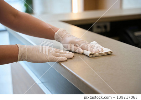 Hands wearing white gloves wiping down a counter with a cloth for hygiene and cleanliness 139217065