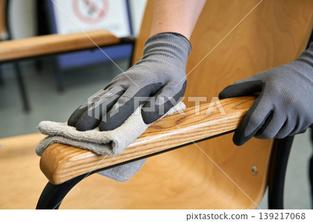Person wearing gloves wipes down a wooden chair armrest with a microfiber cloth 139217068