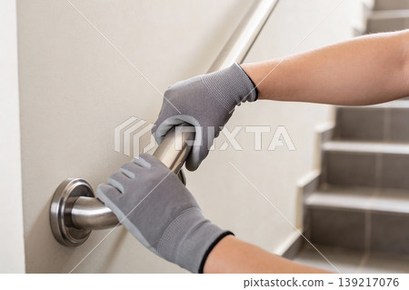Hands wearing grey work gloves installing a stainless steel handrail on a wall Hands wearing grey work gloves installing a stainless steel handrail on a wall 139217076