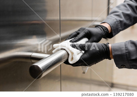 Person in black gloves cleaning a stainless steel handrail with a white cloth 139217080