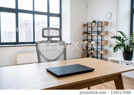 Modern office workspace with a closed laptop on a wooden desk and a comfortable chair Modern office workspace with a closed laptop on a wooden desk and a comfortable chair 139217086