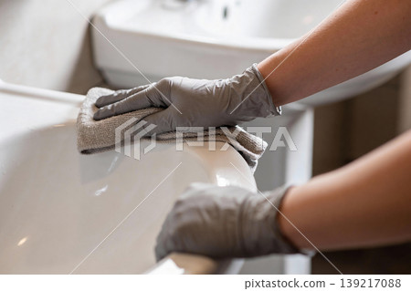 Close-up of hands wearing grey gloves cleaning a white bathtub with a microfiber cloth Close-up of hands wearing grey gloves cleaning a white bathtub with a microfiber cloth 139217088