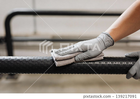 Close-up of a gloved hand wiping down a textured black bar with a microfiber cloth Close-up of a gloved hand wiping down a textured black bar with a microfiber cloth 139217091