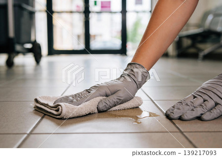 Person wearing gray gloves wipes up a spill on a tiled floor with a cloth Person wearing gray gloves wipes up a spill on a tiled floor with a cloth 139217093