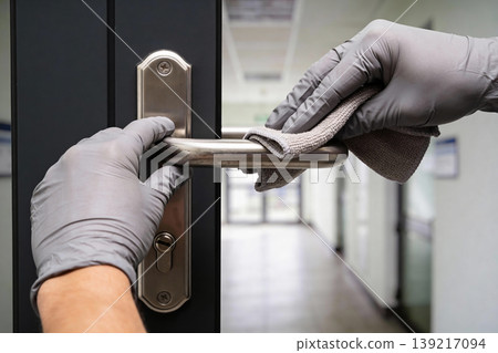 Person wearing grey gloves cleans a metal door handle with a microfiber cloth in a hallway Person wearing grey gloves cleans a metal door handle with a microfiber cloth in a hallway 139217094
