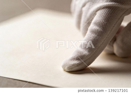 Close-up of a gloved hand gently touching a textured paper surface with soft lighting Close-up of a gloved hand gently touching a textured paper surface with soft lighting 139217101