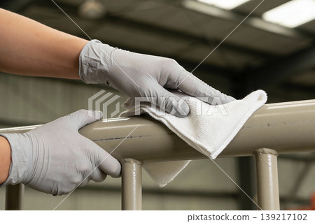 Person wearing gray gloves meticulously cleaning a beige metal railing with a white cloth Person wearing gray gloves meticulously cleaning a beige metal railing with a white cloth 139217102