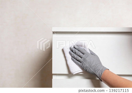 Close-up of a gloved hand wiping down a white surface with a microfiber cloth 139217115