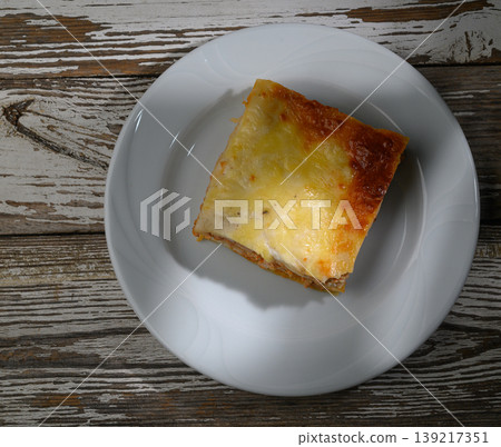 Savory slice of baked lasagna served on a white plate with rustic wooden background 139217351