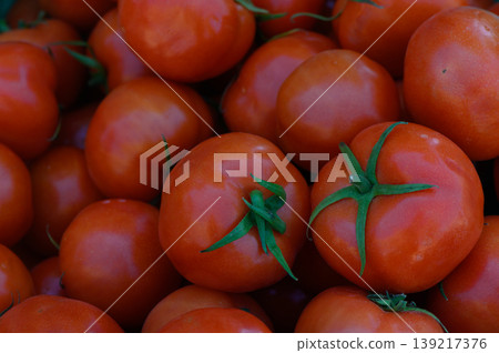 Freshly harvested tomatoes shine bright under the sun, showcasing their vibrant red color and lush green stems at a local farm market 139217376