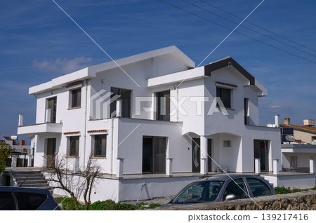 Modern white house under a bright blue sky in a serene neighborhood setting Modern white house under a bright blue sky in a serene neighborhood setting 139217416