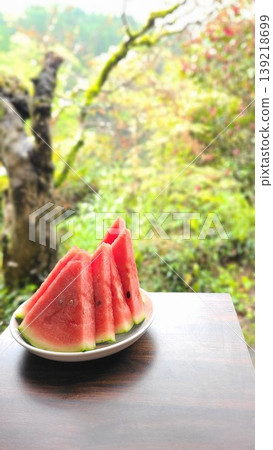 A chilled watermelon against a green background, evoking the feeling of summer; an image of relaxing on a veranda. A chilled watermelon against a green background, evoking the feeling of summer; an image of relaxing on a veranda. 139218699