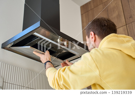 Man removing filter from modern kitchen hood for cleaning Man removing filter from modern kitchen hood for cleaning 139219339